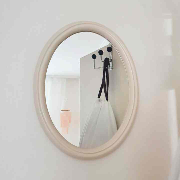 ベージュ色の壁にベージュのフレームの楕円形の鏡が掛けられている落ち着いた印象の空間