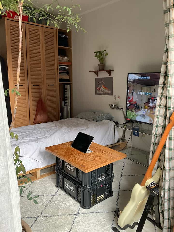 ナチュラルカラーの寝室とリビングが融合した空間、木製ベッドとクローゼットが配置され、温かみのある雰囲気のインテリア