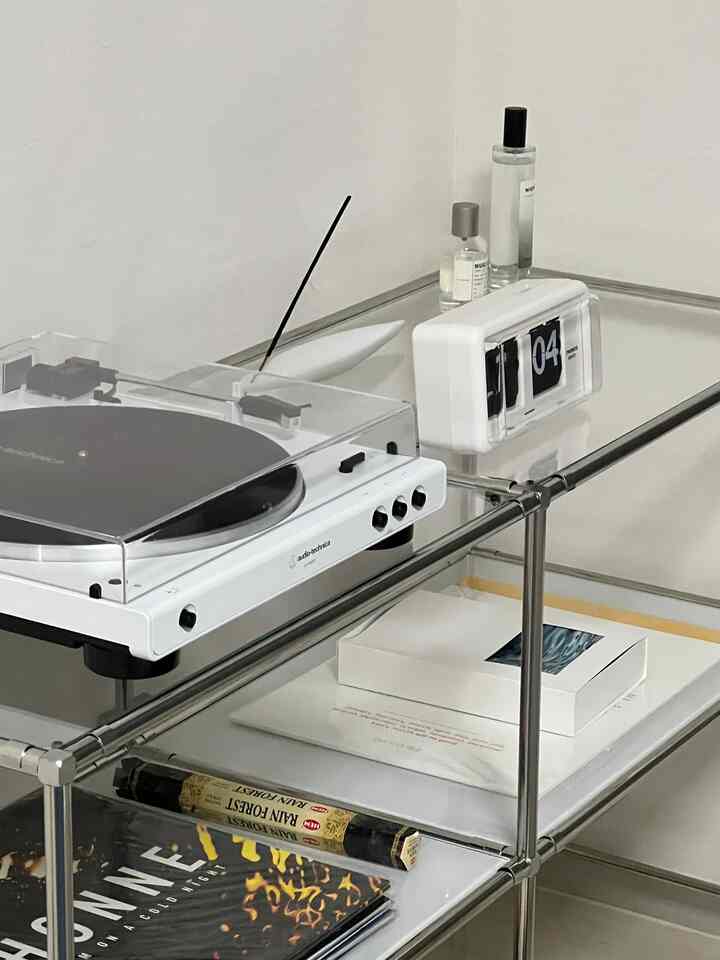 白とメタル素材の棚にターンテーブル、フリップクロック、お香スティックなどが配されたモダンで洗練されたインテリアスペース