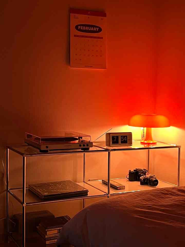オレンジ色の照明が灯る寝室の棚にヴィンテージのターンテーブルとカメラが配置された雰囲気のあるインテリア