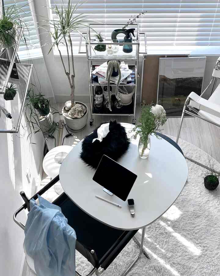 白とシルバーを基調としたモダンなホームオフィス、中央にデスクと植物、小さなトロリーが配置された明るく整ったインテリア