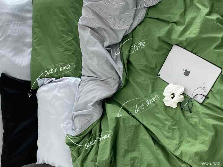 深い緑色とストライプ柄の寝具が配置された寝室、サテンの黒と銀のカバーがスタイリッシュで温かみのあるインテリア