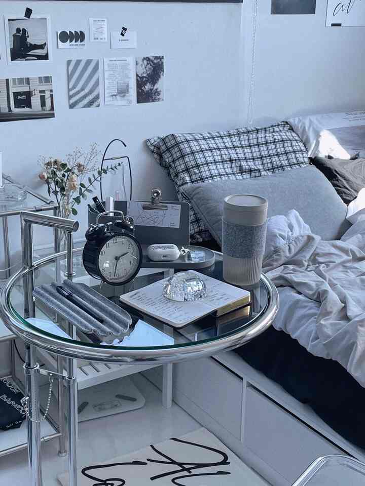 白とグレーのトーンでまとめられたコンパクトな寝室、丸いガラスのサイドテーブルと置時計が配置された雰囲気のあるインテリア