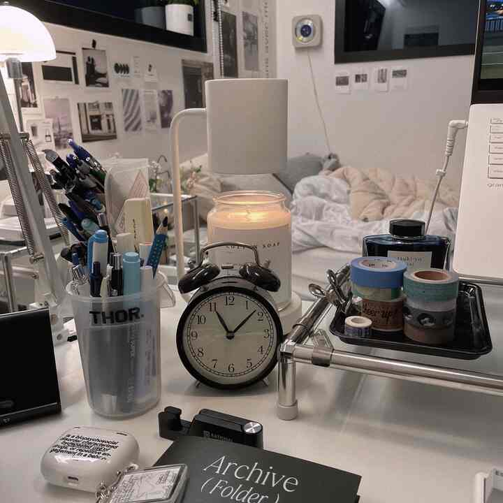 白を基調としたホームオフィスのデスク、黒いアナログ時計とムードランプ、文房具が整ったシンプルな作業空間