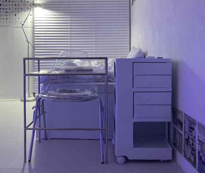 ホワイトとシルバーの6畳の寝室、シンプルモダンなデスクと透明なオフィスチェア、フロアランプが配置された清潔感のあるホームオフィス兼寝室