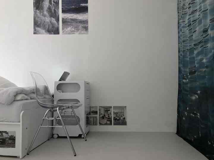 白と青のトーンの寝室、透明な椅子とミッドセンチュリーモダンスタイルの寝具と家具が配置されたシンプルな空間