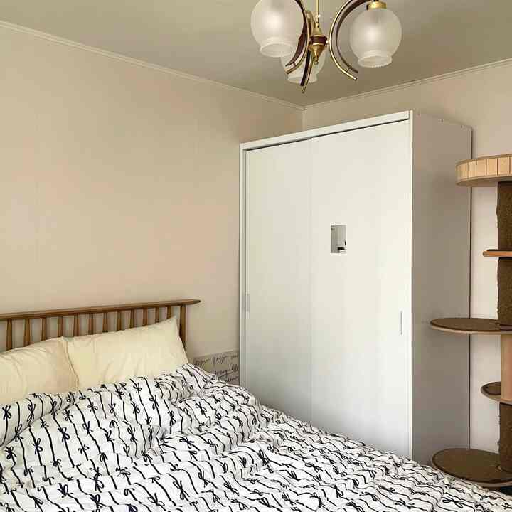 明るいホワイトとナチュラルブラウン調の寝室、クイーンサイズベッドと白いワードローブ、木製キャットタワーが配置された温かみのある空間