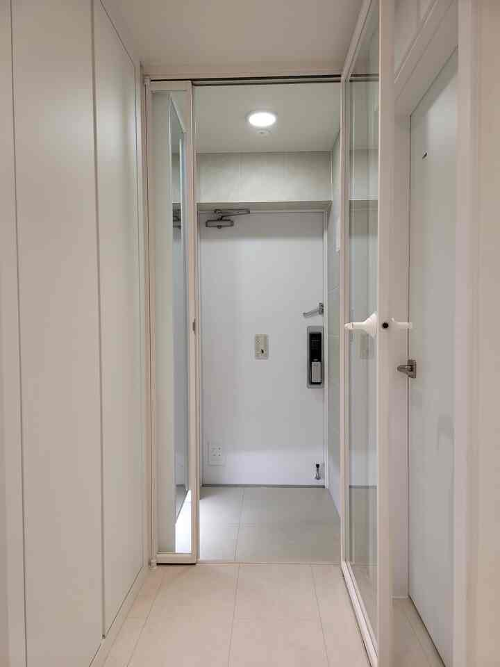 ホワイトトーンの狭くてシンプルな玄関、透明な中扉と靴箱が配置され、広く見えるインテリア