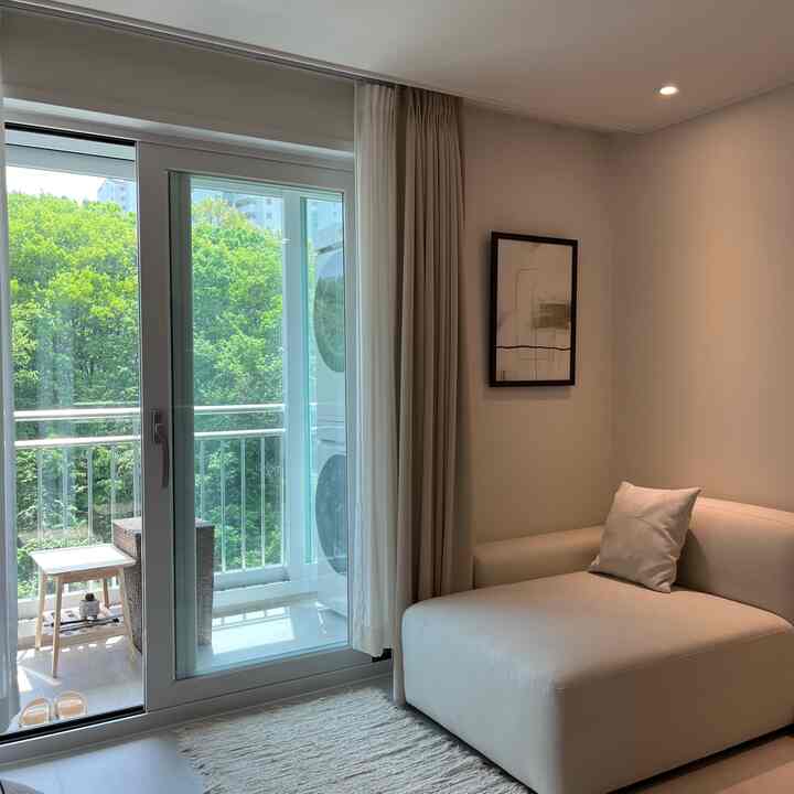 白とベージュの色調のリビング、ソファとカーテン、ベランダの扉が配置された落ち着いた自然な雰囲気のインテリア