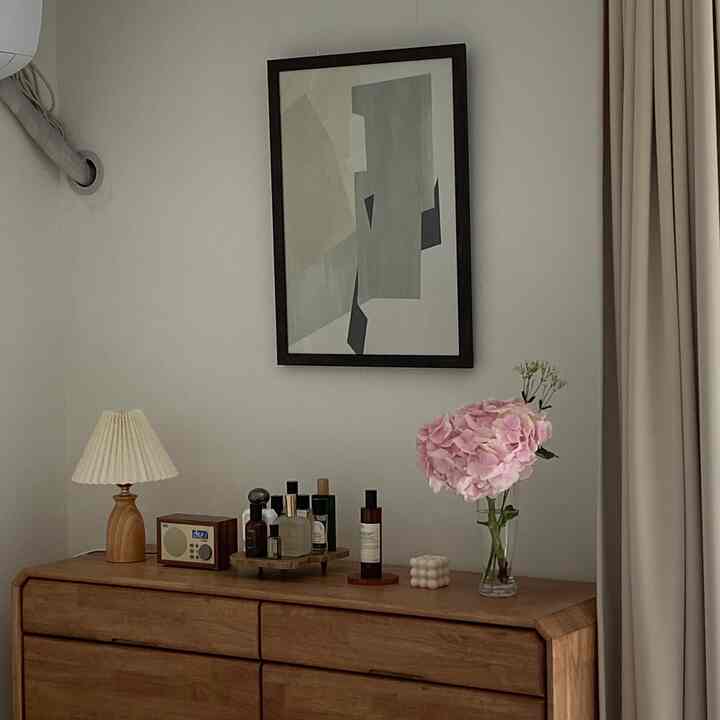 落ち着いた白と茶色のトーンの寝室のチェスト空間、木製のデスクランプと香水瓶、花瓶が調和するナチュラルなインテリア