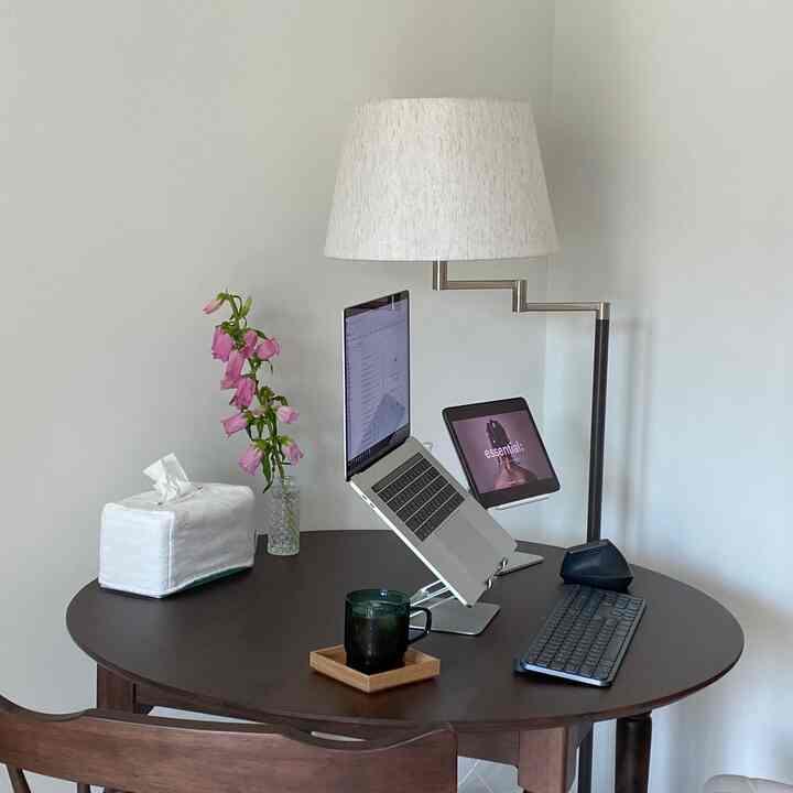 白い壁と木目調の丸テーブルが配置された落ち着いたホームオフィス空間、フロアランプとデジタル機器が置かれた雰囲気のあるインテリア