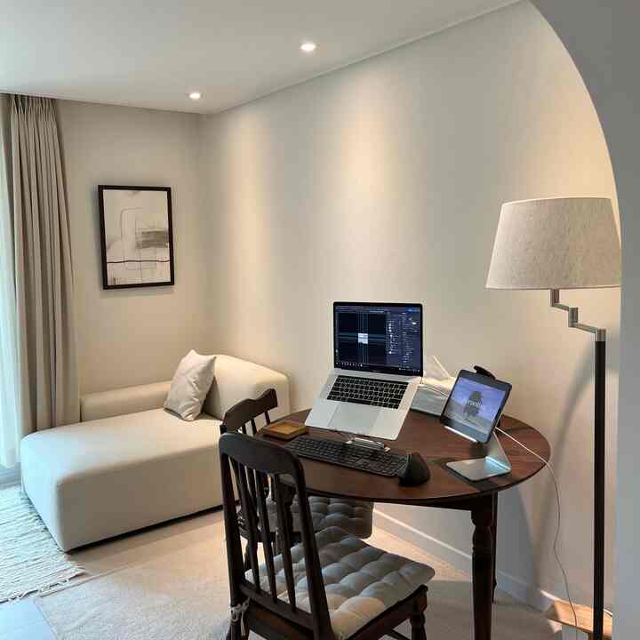 ベージュトーンのホームオフィス、ダークブラウンのダイニングテーブルとソファが配置されたシンプルで落ち着いた作業空間