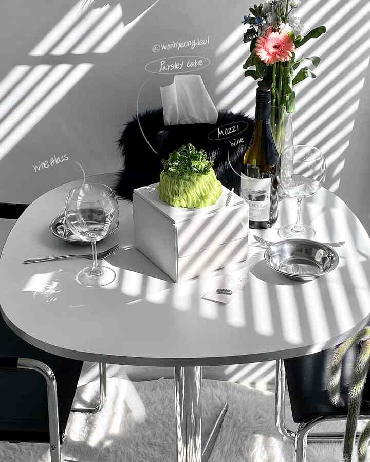 白を基調としたワンルームのリビング、中央に白いダイニングテーブルと黒いチェアが配置されたモダンで清潔感のあるインテリア