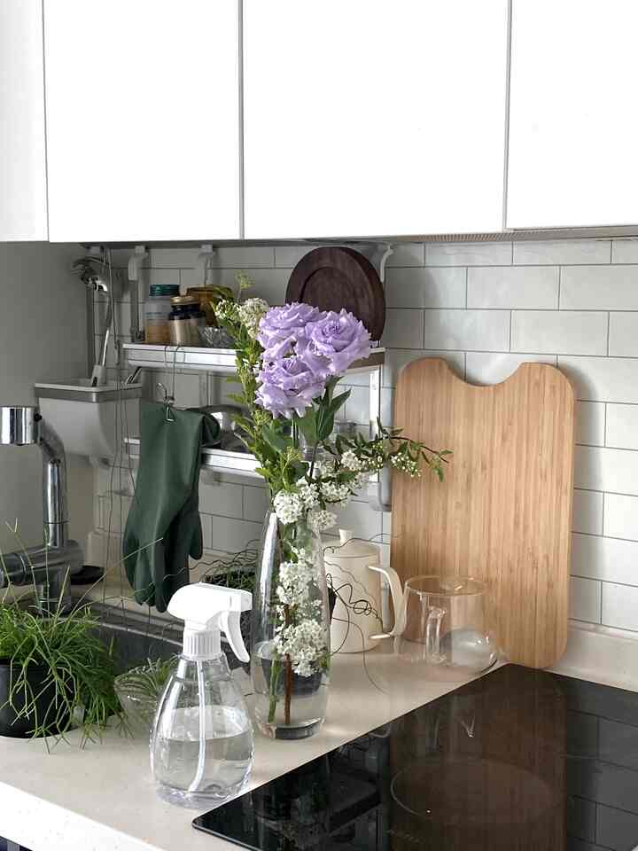 白いタイル壁とナチュラルな木製まな板、花瓶に入った紫の花と植物が配置されたシンプルなキッチンの空間