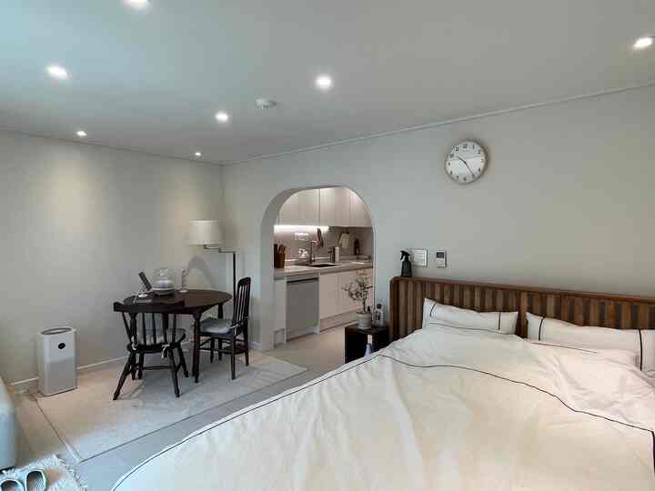 ホワイトとブラウンのウッドトーンが調和したワンルームの寝室とキッチン、落ち着いた清潔感のある空間