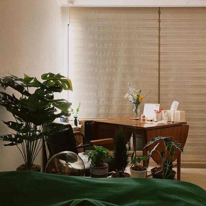 ナチュラルでブラウン調の寝室、窓際に配置されたダイニングテーブルと多くの植物がある雰囲気のあるインテリア