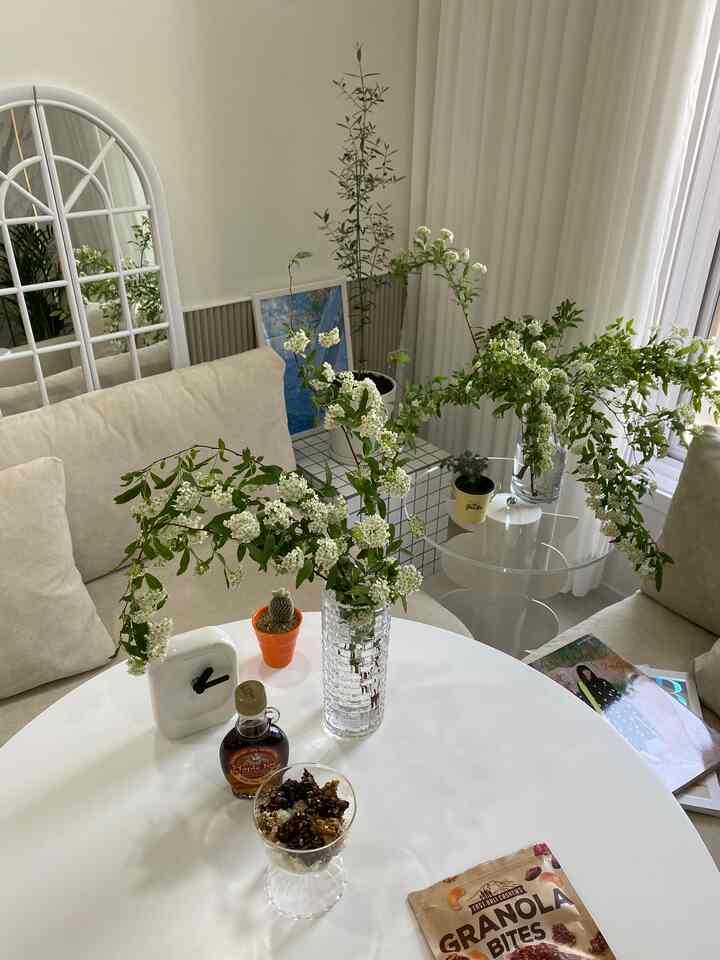 明るい白とベージュの寝室、丸テーブルとベージュのソファ、額縁と緑の植物が配置されたナチュラルな雰囲気のインテリア