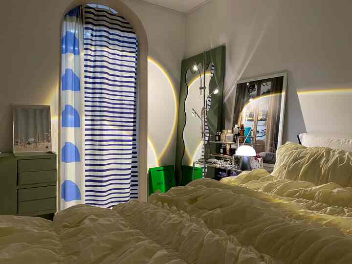 黄色い寝具と青いストライプのカーテンがある温かみのある寝室、全身鏡と照明が配置された雰囲気のあるインテリア