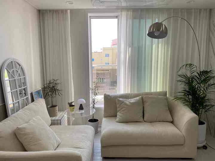 ナチュラルな色調のリビング、クリーム色のソファとシルバーのフロアランプ、多様な植物が配置された雰囲気のあるインテリア