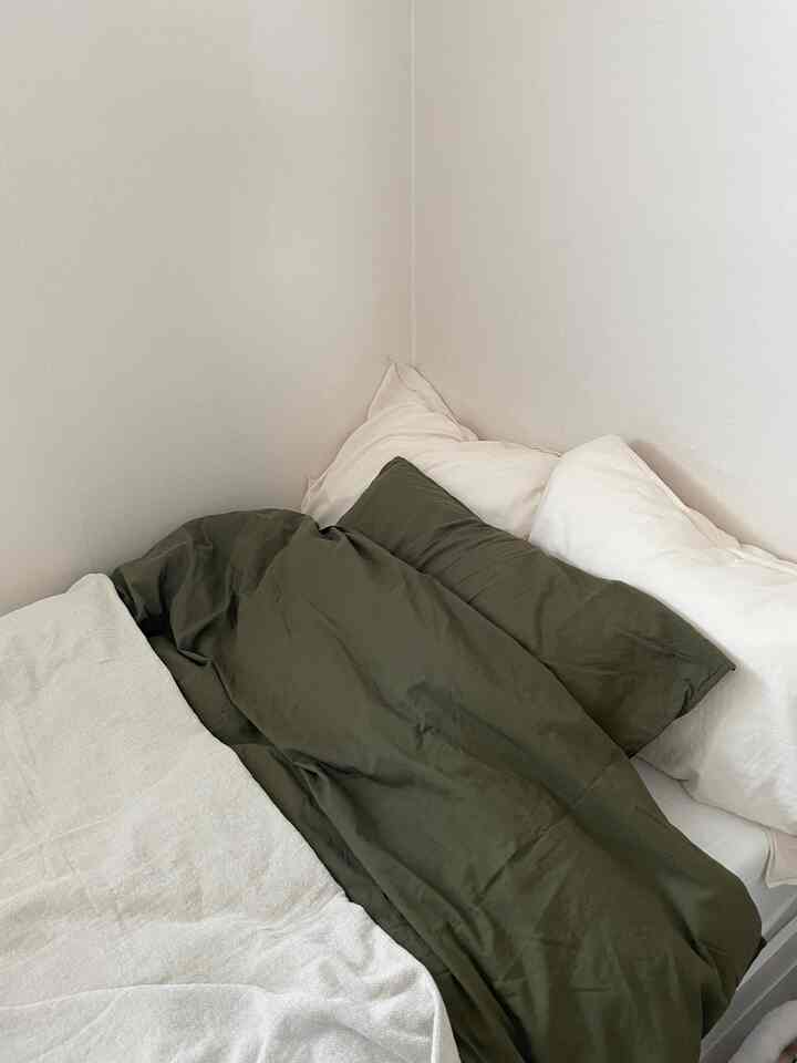 明るい白い壁と濃い緑の寝具が調和する落ち着いた寝室のインテリア