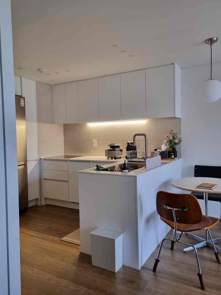 ホワイトとブラウンのトーンが特徴的なL字型キッチン、丸いダイニングテーブルとチェアが配置された清潔感のあるナチュラルモダンなインテリア