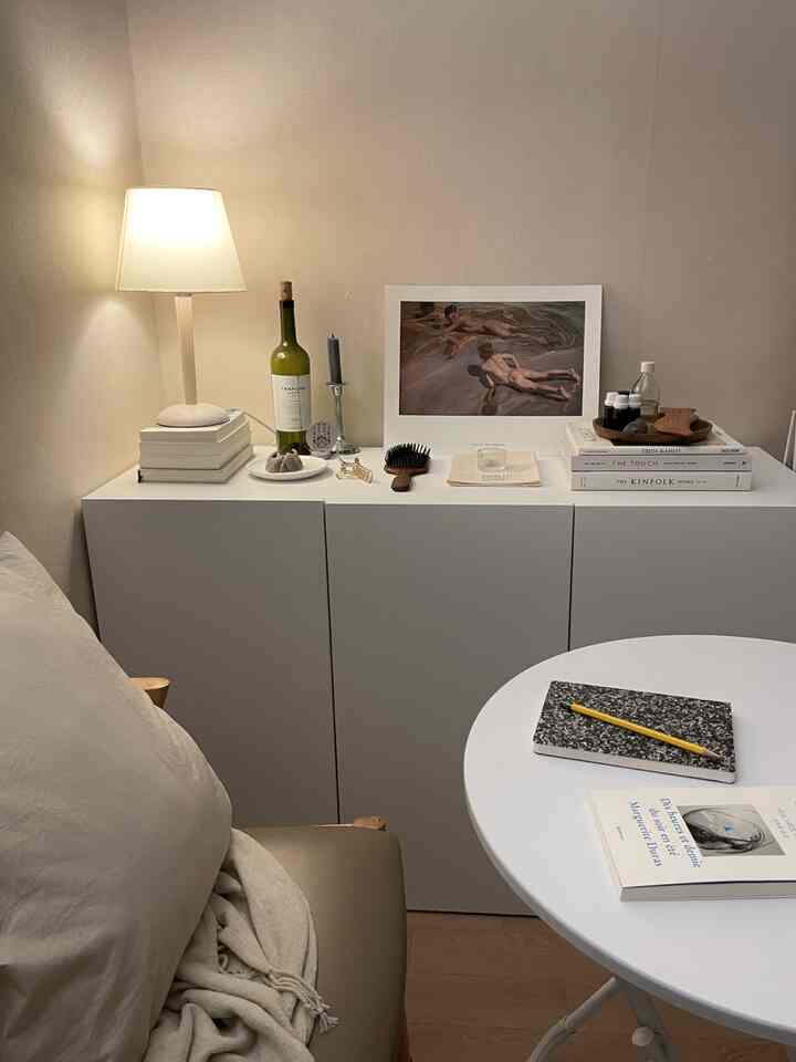 ベージュの壁とホワイトのキャビネットが配されたナチュラルトーンのリビングコーナー、オブジェと照明が調和する温かみのある空間