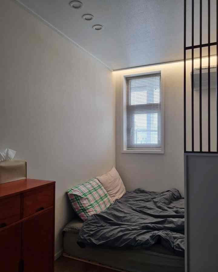 白を基調とした狭い寝室、コンパクトなベッドとブラインドが配置されたミニマルでナチュラルな雰囲気のインテリア