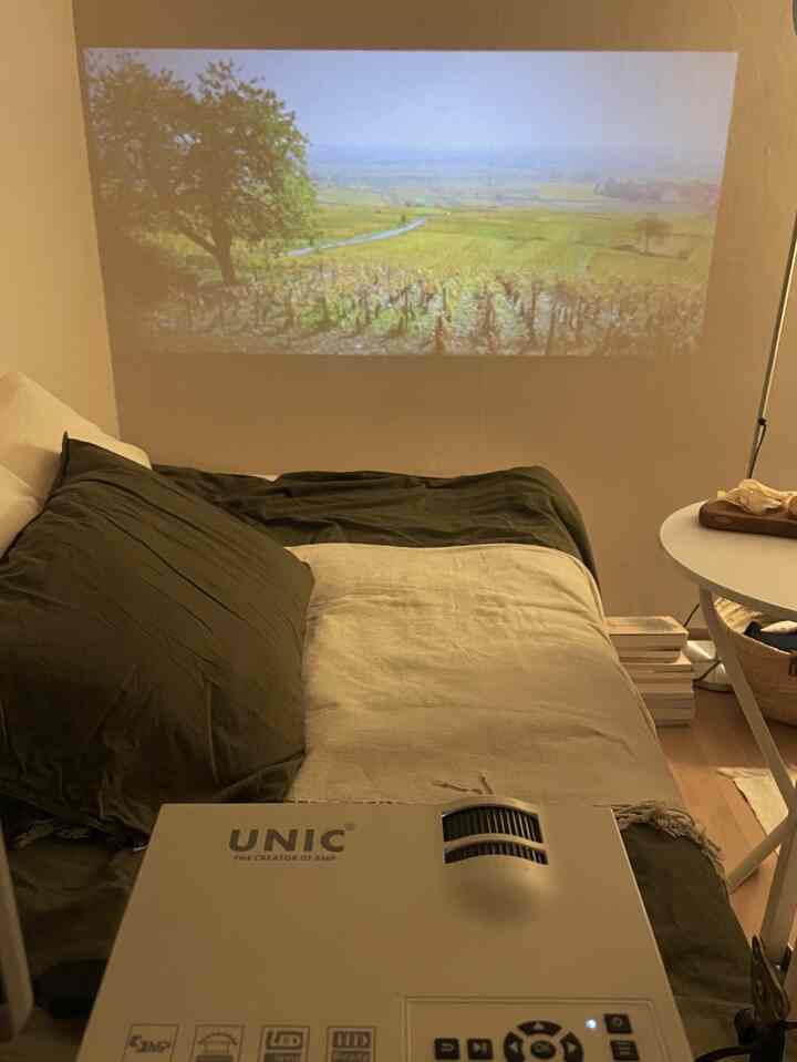 白い壁と緑のスローがある寝室、壁に映像を映すプロジェクターのある雰囲気のホームシネマ空間