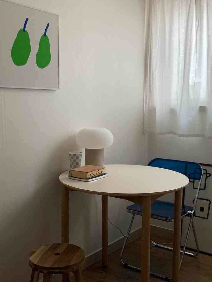 白とナチュラルウッドトーンの調和が取れた、小さな円形テーブルとスツール、透明な青い椅子が配置された空間