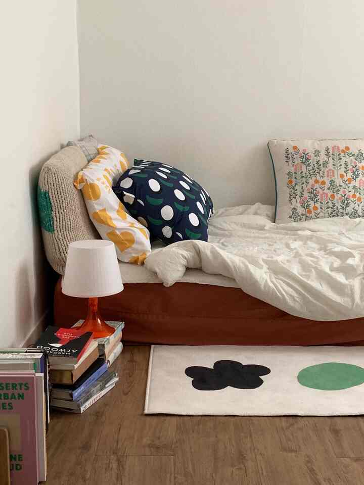 ナチュラルカラーのコンパクトな寝室、フレームなしベッドと多様な柄の枕が配置された落ち着いた雰囲気の空間