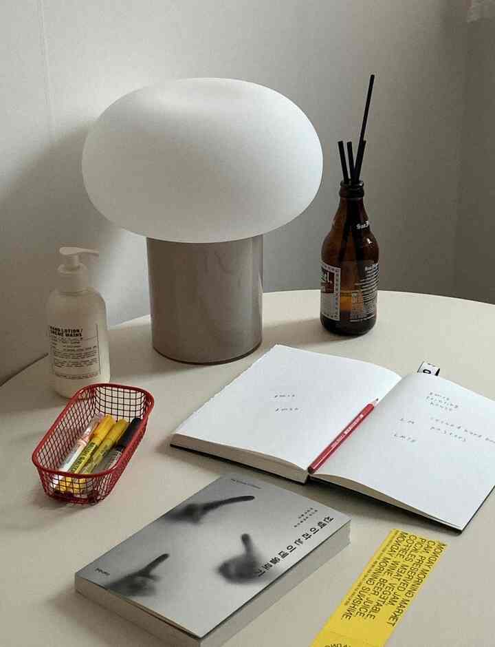 落ち着いたホワイトトーンのデスク上に白いテーブルランプとブラウン色のディフューザー、ペンと本が配置されたミニマルなインテリア