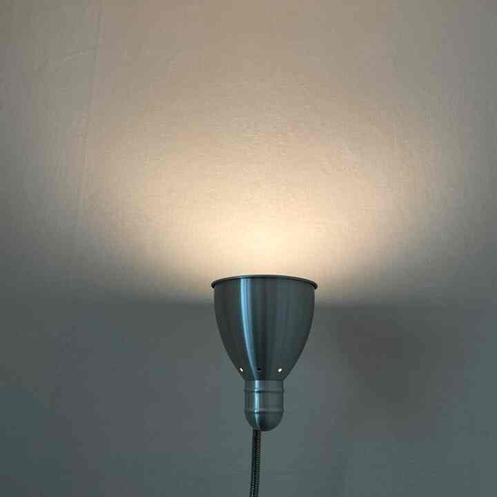 柔らかな照明が照らすシルバーのフロアランプがあるモダンな寝室の壁面