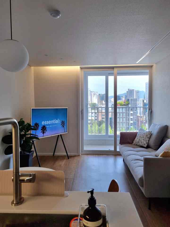 ベージュの壁と木目調の床が調和するアパートのリビングとキッチン、テレビとソファが配置された温かみのある空間