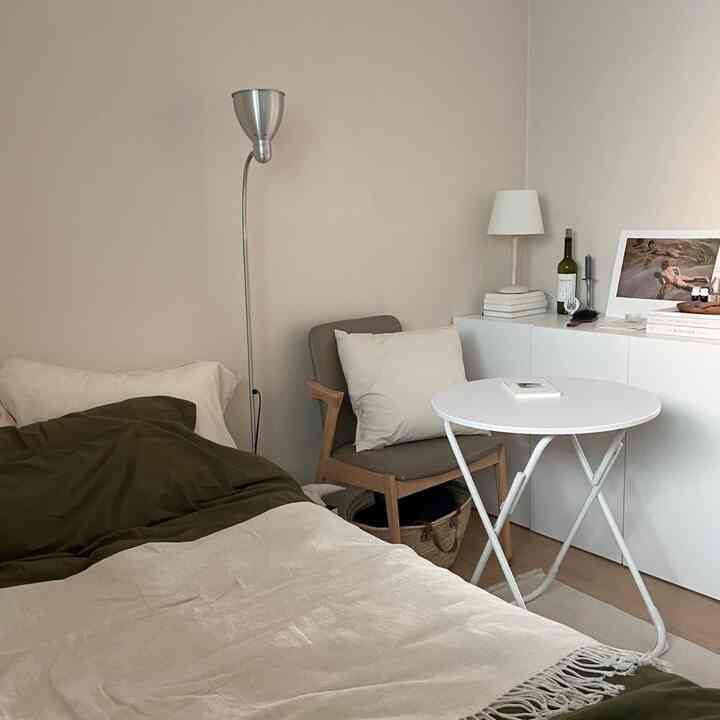 ベージュとホワイトの落ち着いた寝室、ベッドとアームチェア、照明、ホワイトテーブルが配置されたミニマルで清潔感のある空間