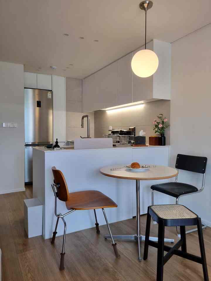 白と木目調の小さなモダンなキッチン、丸テーブルと異なる椅子が配置された雰囲気のある空間