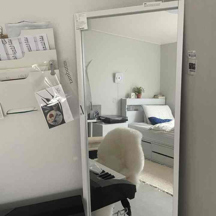 白と青のトーンが調和したシンプルな寝室、ベッドと全身鏡、整然とした収納家具が配置された空間