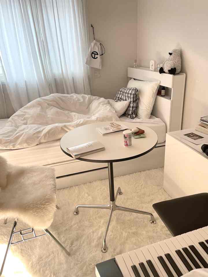 ホワイトトーンのワンルーム寝室、丸テーブルと暖かいラグが配置されたシンプルモダンなインテリア