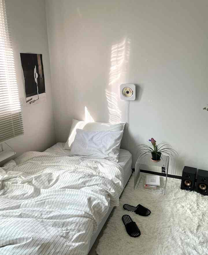 白やグレーのモノトーンでまとめられた、シンプルなベッドとラグが配置されたコンパクトで清潔感のあるホームオフィス兼寝室