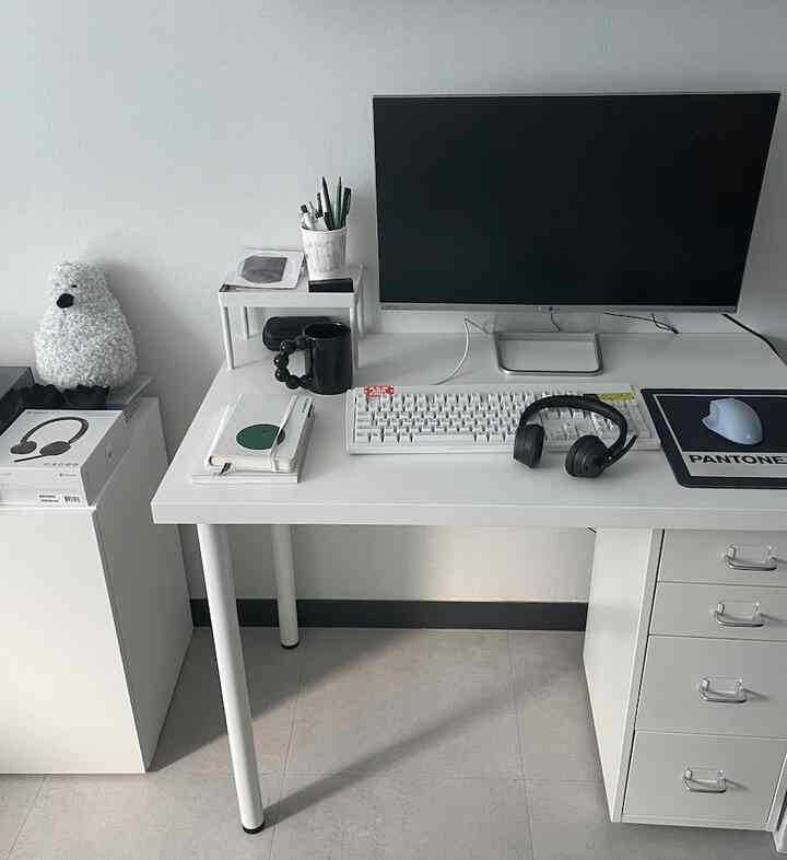 白を基調としたホームオフィス、モニターとキーボードが置かれたデスクとヘッドセットのあるシンプルな作業空間