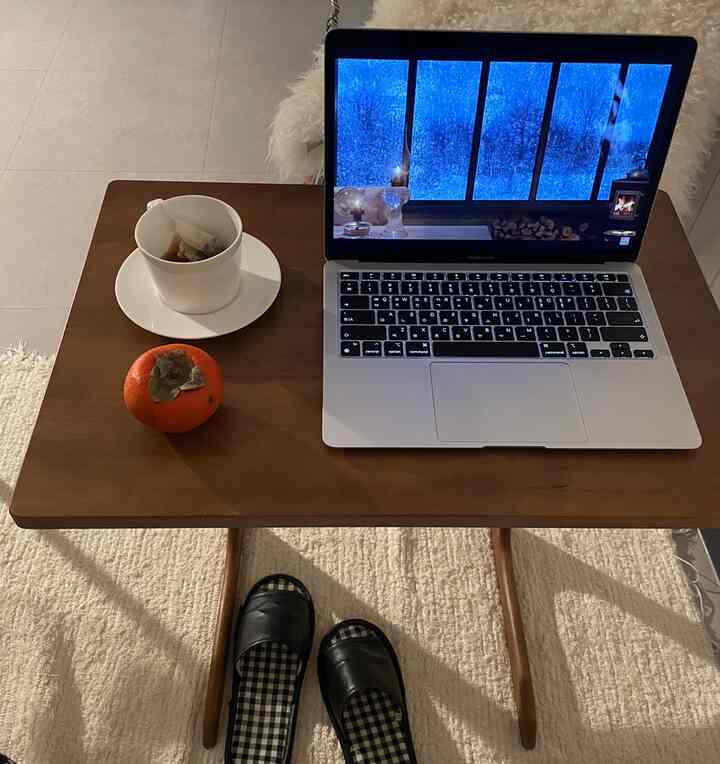 ナチュラルな色調のサイドテーブルの上にアップルのマックブックエアとコーヒーカップ、柿が置かれた落ち着いたおうちカフェの空間