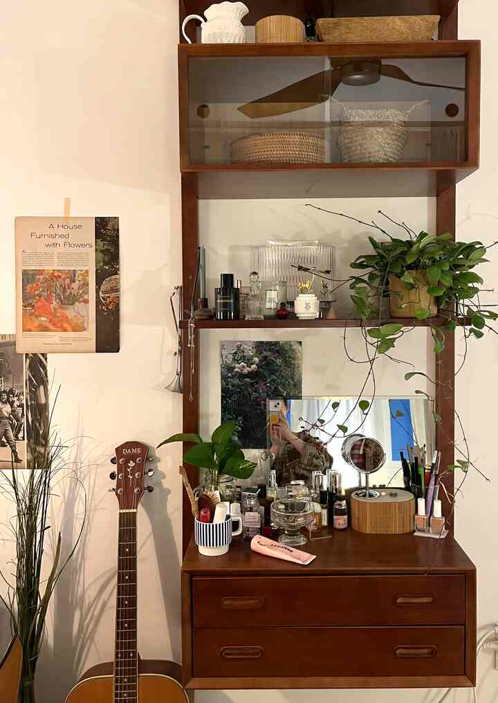 ナチュラルな木目調と緑の観葉植物が配された化粧台とモジュラー棚のある雰囲気のある空間