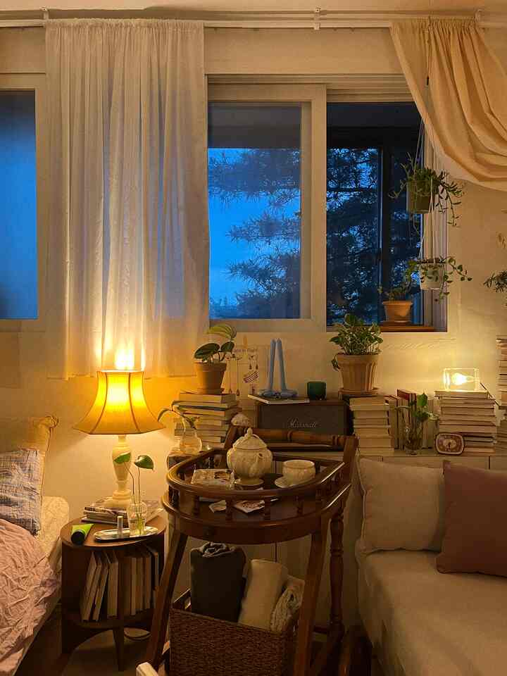 暖色の照明に照らされた木製家具とベージュのソファ、夜の青い空が見える窓が調和した居心地の良いリビング