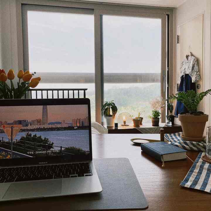 白と茶色の自然な色調の空間、バルコニーの眺めがあり、ノートパソコンと植物が置かれた居心地の良いホームオフィス