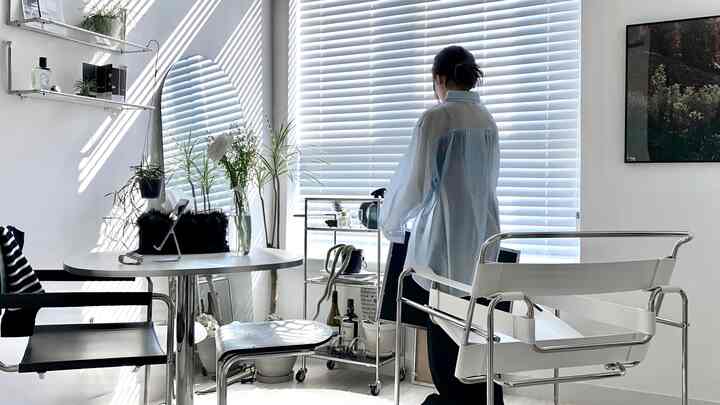 ホワイトトーンのミニマルなリビング、広いブラインドと小さな植物、シンプルな家具が配置された採光の良い空間