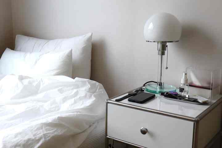 白を基調とした寝室、白い寝具とモジュールナイトテーブルの上にテーブルランプが置かれたシンプルでホテルライクな雰囲気のインテリア