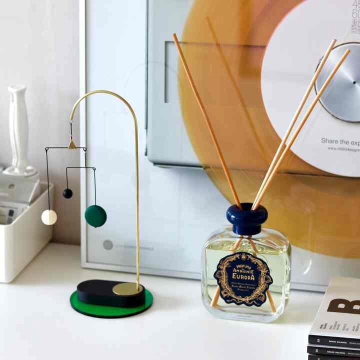 ホワイトとブルーの色調の背景にミニマルなテーブル上のディフューザーとカラフルなモビールが配置された雰囲気のあるインテリア