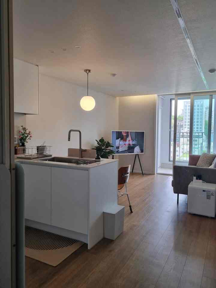 ホワイトとウッドトーンの小さな玄関口から見えるモダンなキッチンとリビング空間、ペンダントライトとテレビ台が配置されたすっきりとした開放感のあるインテリア