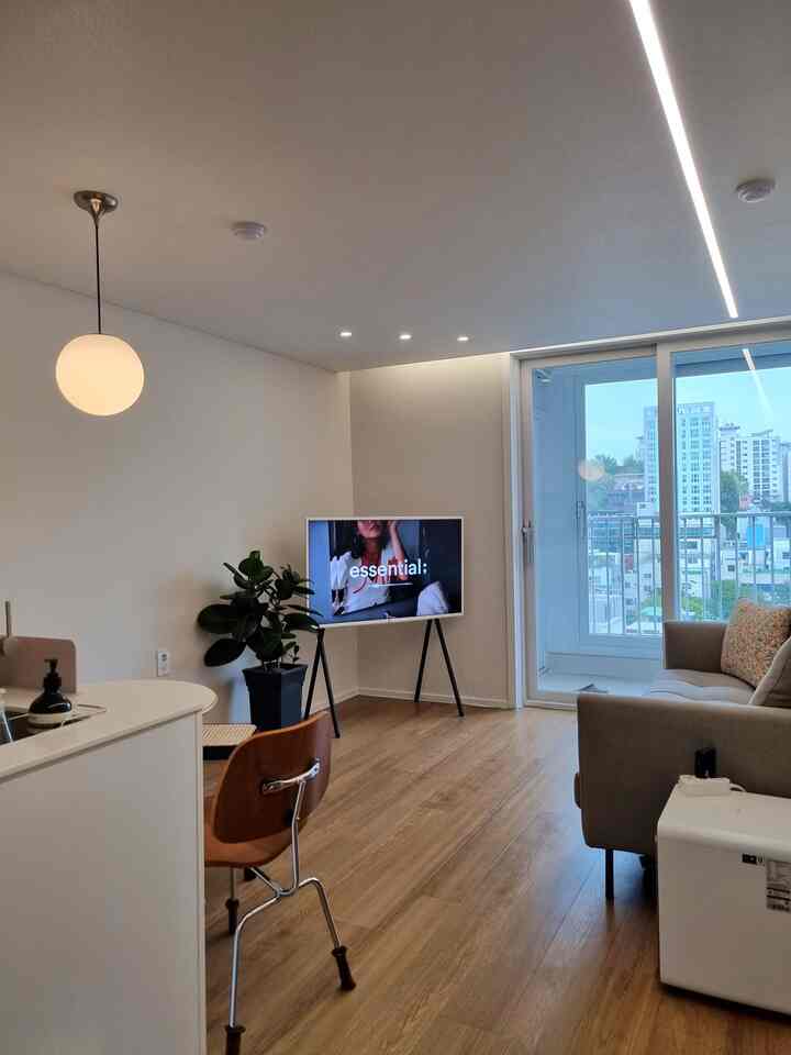 白い壁と木目調の床のワンルームリビング、ソファとテレビ台が配置された自然な雰囲気の空間