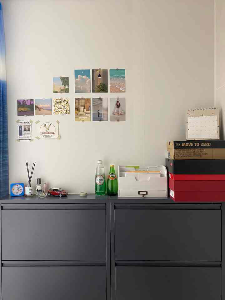 白い壁と黒のシューズラックがある玄関空間、壁に小さな写真が貼られ、ラックの上に小物や靴箱が積まれている印象的なインテリア