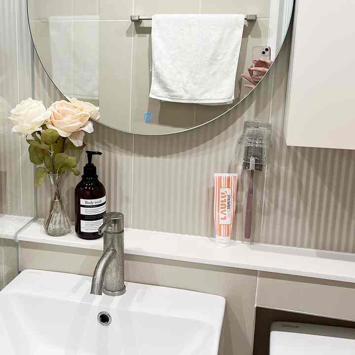 白とベージュの色調のバスルーム、洗面台と丸い鏡、清潔なタオルとミニマルな小物が配置されたモダンな空間